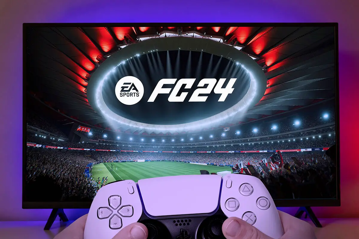 Boy playing EA FC 24 with Playstation 5 controller on TV screen.