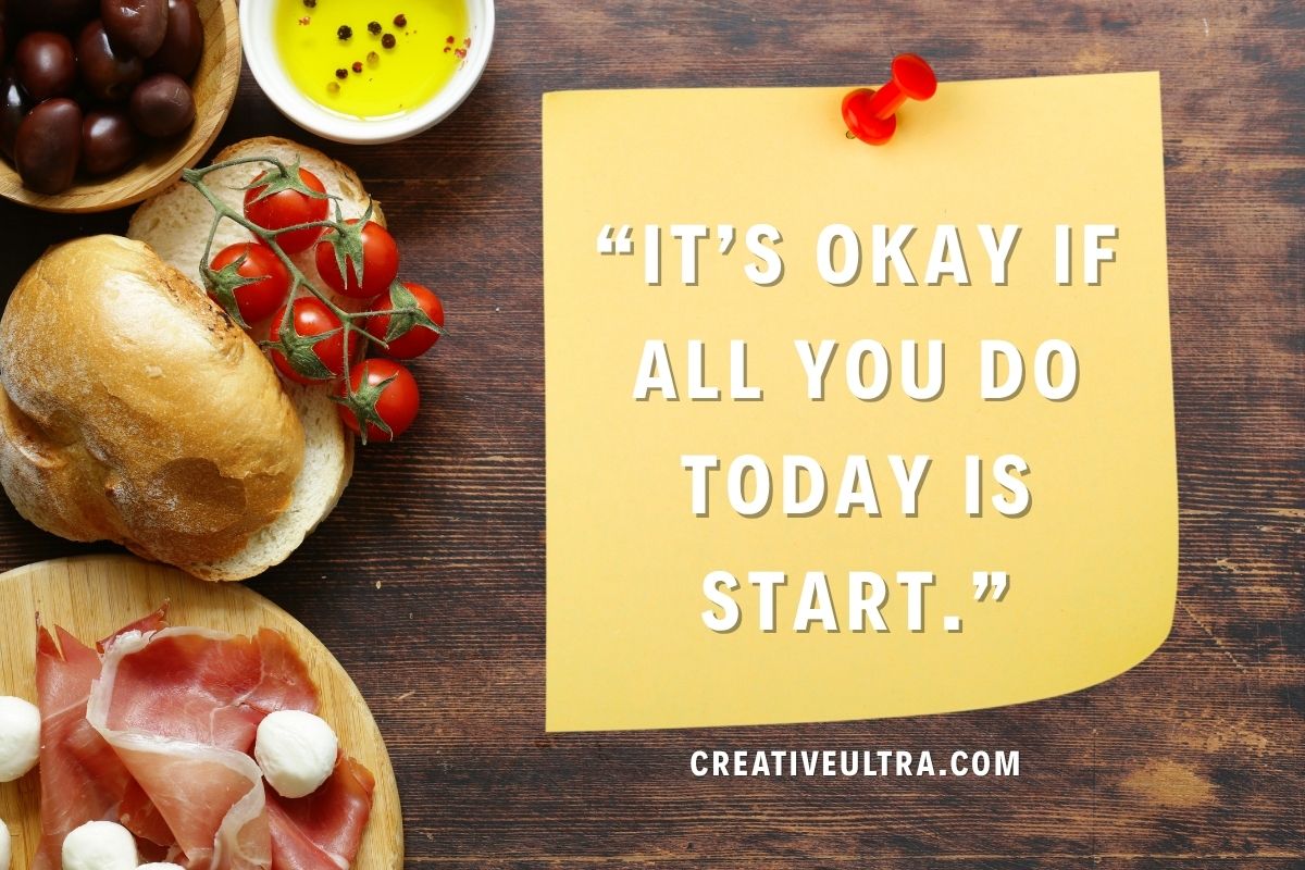 Yellow note reads, “It’s okay if all you do today is start,” pinned on wood. Nearby are cherry tomatoes, bread, ham, mozzarella, and olives, evoking warmth.