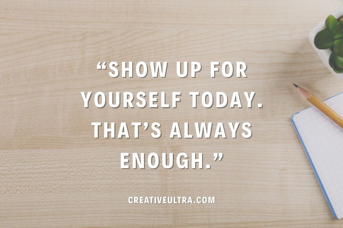 Inspirational quote on a wooden desk background reads, "Show up for yourself today. That's always enough." Nearby are a pencil, notepad, and small plant.